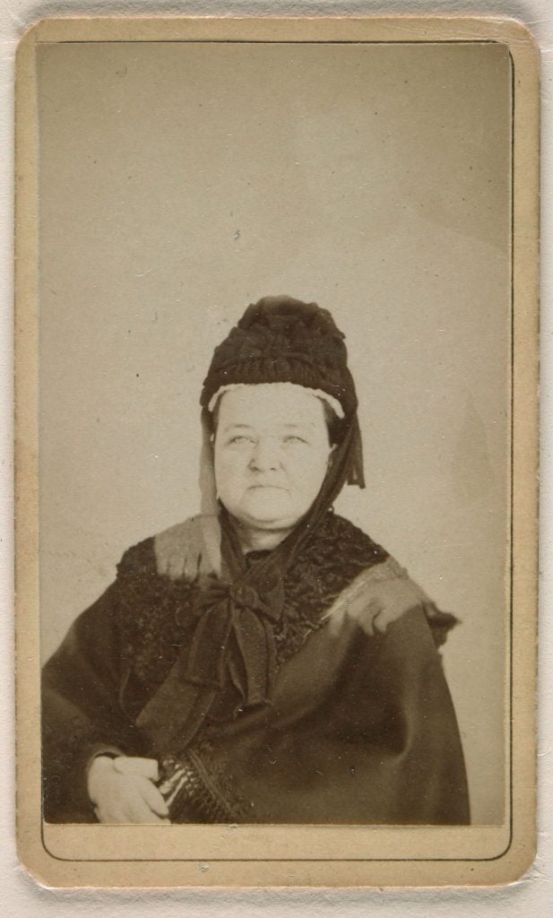 Double exposure photo of Mary Todd Lincoln posing in black cape and bonnet, with a white figure of Abraham Lincoln behind her